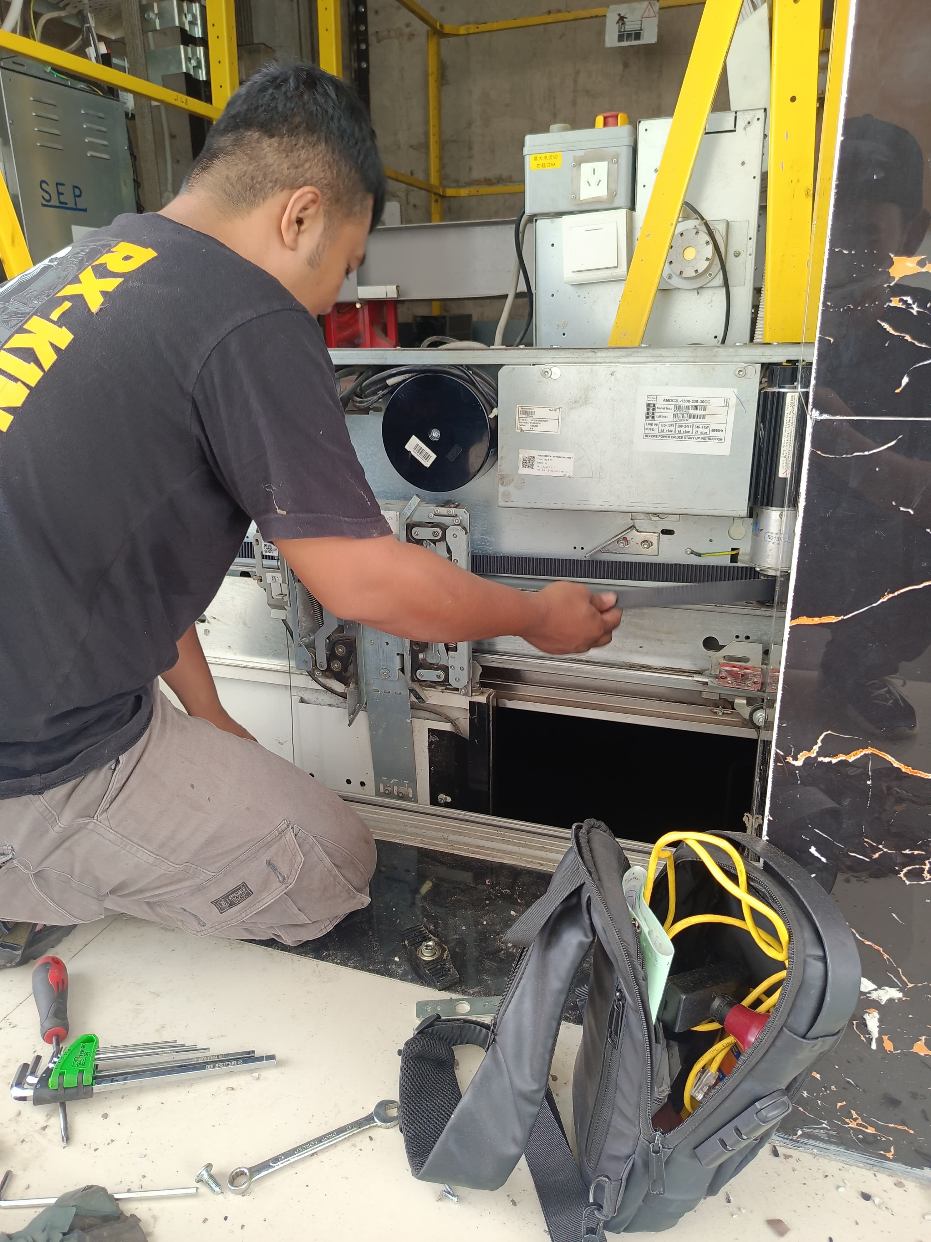 Teknisi mengganti komponen eskalator dengan alat khusus di pusat perbelanjaan, latar biru muda
