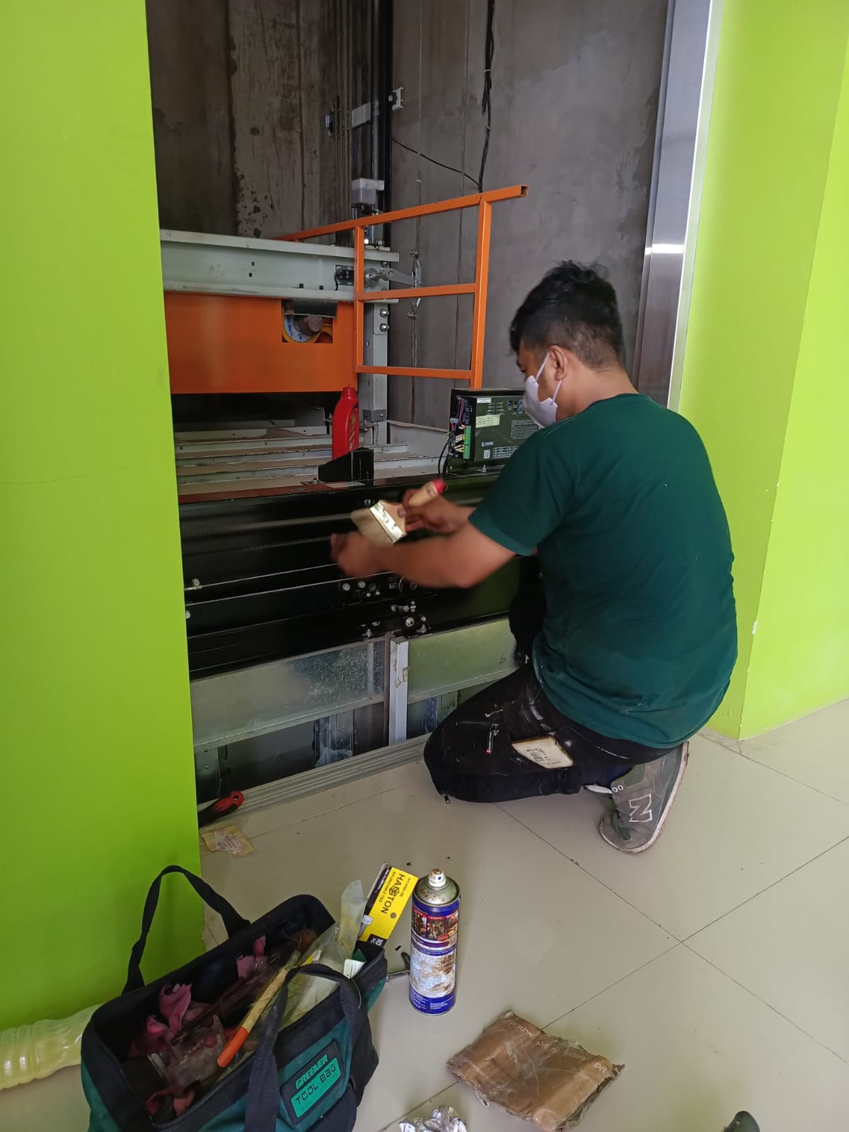 Teknisi sedang memeriksa kondisi lift di gedung perkantoran modern dengan alat pengukur, latar biru cerah