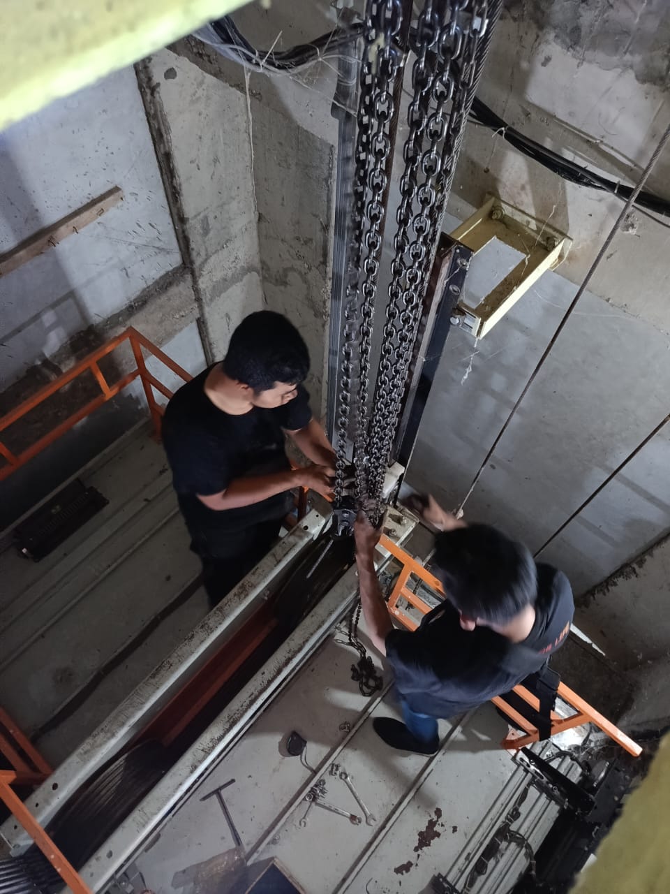 Teknisi melakukan pemeriksaan keselamatan lift dengan alat pengukur di gedung perkantoran, latar biru lembut